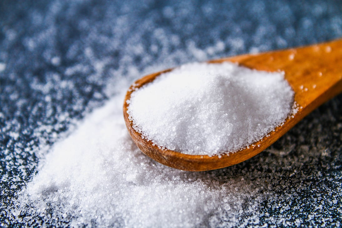 Crystals of shallow salt in a scoop, spoon on a dark gray table. Background for advertising salt. Table salty. Salted food.