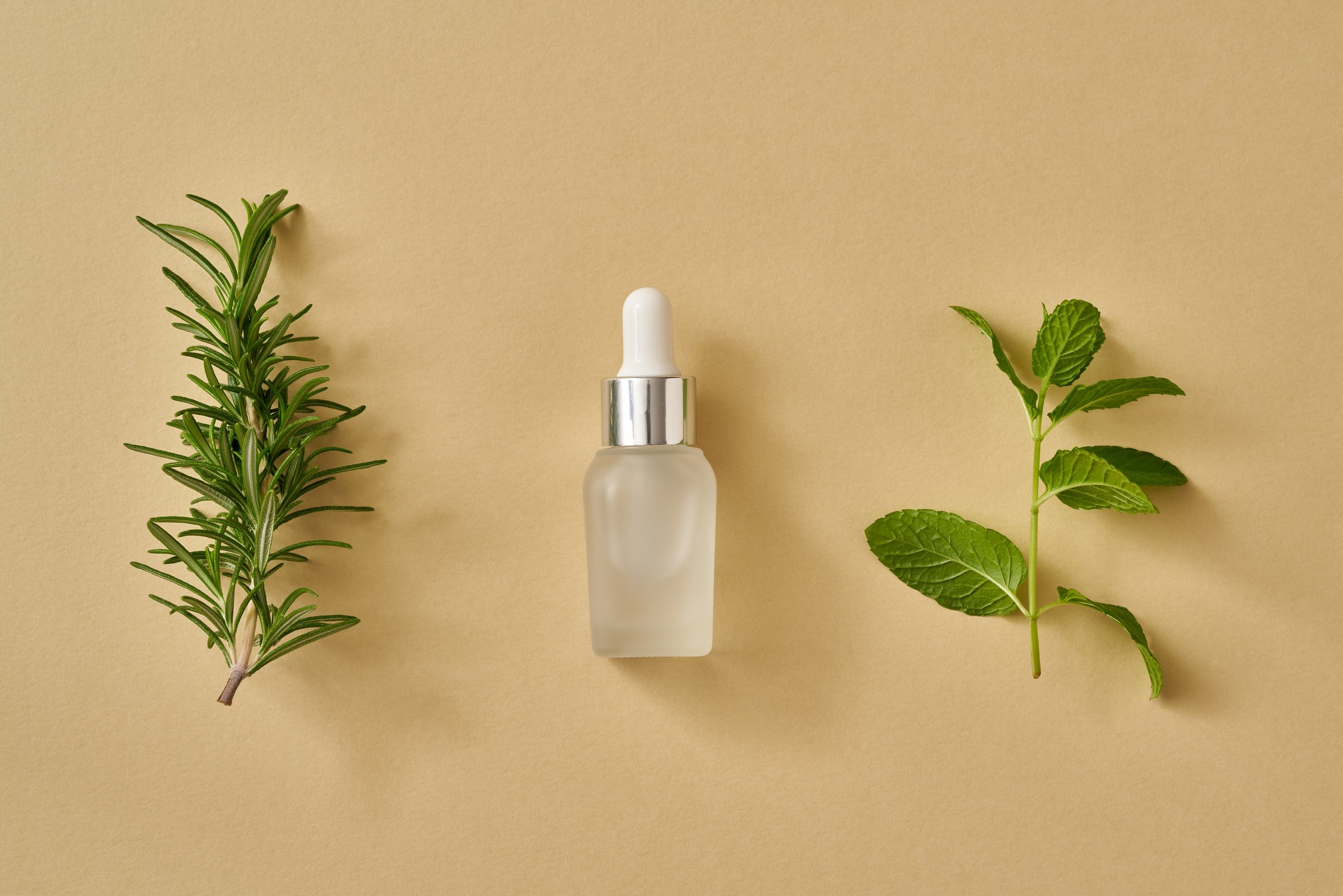 A bottle of essential oil with fresh peppermint and rosemary leaves